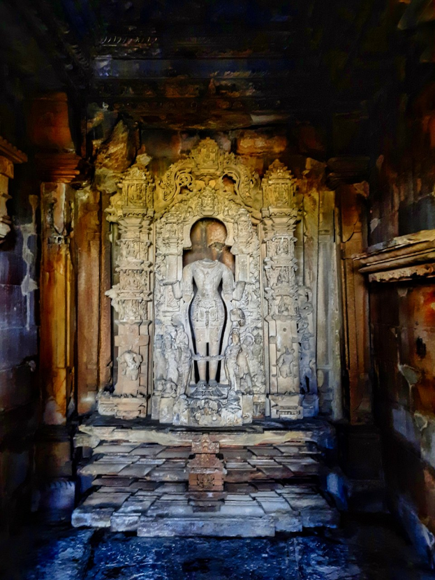 Ancient Hindu temple interior in India featuring a central statue, intricate wall and pillar carvings, and visible flooring.