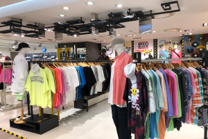 Ein Bekleidungsgeschäft im Mall of Asia mit Schaufensterpuppen in Mützen, Kleidung an Bügeln, Schautafeln mit Text und Deckenleuchten.