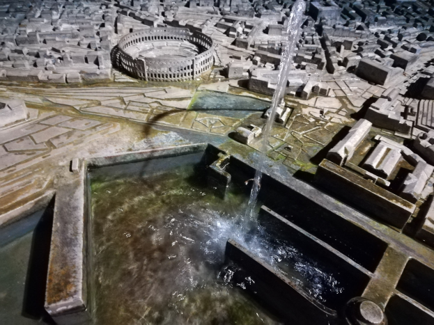 Ein Miniaturstadtmodell mit einem zentralen Springbrunnen mit Wasserfall, umgeben von Gebäuden und Wasserfeatures.