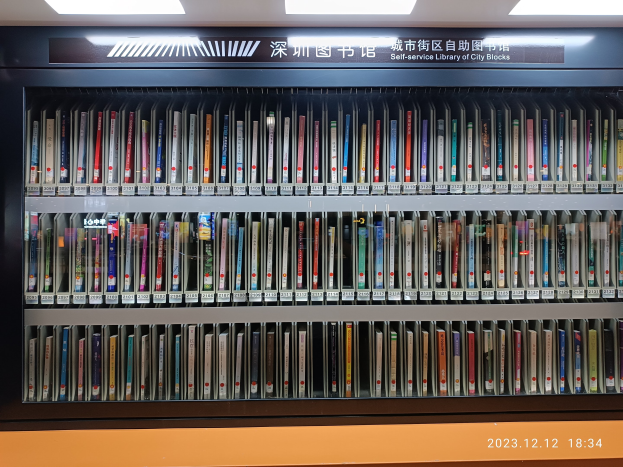 Eine gut beleuchtete Bibliothek mit hohen Bücherregalen, die mit Büchern gefüllt sind, ein Textschild und ein Wasserzeichen unten, das einer Selbstbedienungsbibliothek der Stadtblocks ähnelt.