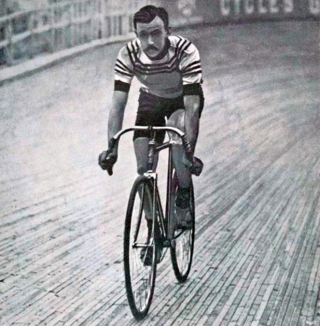 Schwarz-weiß-Foto eines Mannes, der auf einer Bahn mit einem Zaun und einer Tafel im Hintergrund Fahrrad fährt, der angeblich Sir Ernest Hemingway ist.