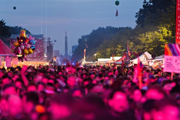 Eine große Menge bei einem nächtlichen Musikfestival mit farbigen Lichtern und Ballons, umgeben von Zelten, Bannern, Fahnen, Bäumen, einem Turm und einem sternenklaren Himmel.
